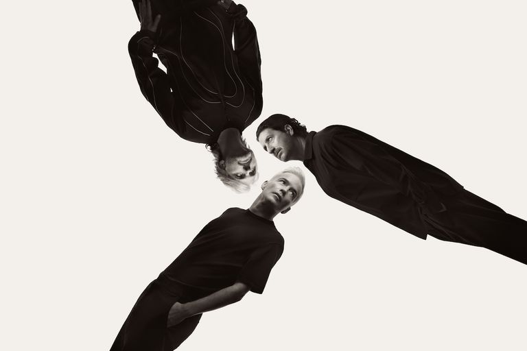 Black and white photo of electronic music group The Avalanches, featuring three band members angled inward against a stark white background.